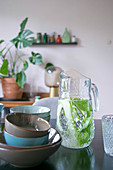 Bowls in earthy shades next to carafe of water, cucumber and mint