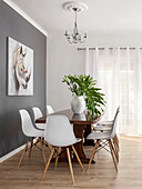 weiße Designerstühle um einen Holztisch vor grauer Wand