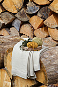 Wool and knitting needles on wooden board in front of stacked firewood