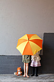 Two girls hiding behind yellow and orange umbrella