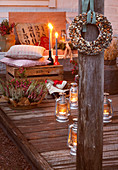 Wreath of bird seed hung on wooden pillar in front of lanterns on floor, cushions on wooden crate and candles on terrace