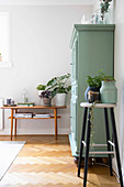 Plants on bar stools and console table flanking green cabinet