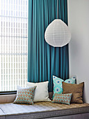 Bench with cushions and hanging lamp in front of window with blue curtain