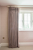Grey curtain draped in elegant folds against spotted wallpaper