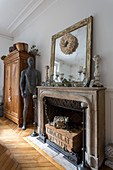 Mirror on mantelpiece above fireplace, sculpture and wooden cupboard in living room