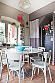 Round table, wooden chairs and fridge with chalkboard paint in niche in kitchen