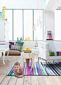 Baby lying on rug in white living room with brightly striped accessories