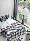 Blick auf Doppelbett mit schwarz-weiß gemusterter Tagesdecke und gestreiften Kissen vor Terrassentür