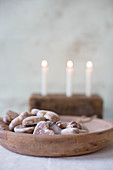 Holzschale mit Lebkuchenherzen, im Hintergrund drei brennende Kerzen