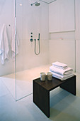 Towels and beakers on stool next to shower area with glass screen