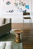 Designer-Beistelltisch aus Holz neben Sofa, im Hintergrund Stuhl vor moderner Fotomontage