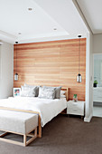 Double bed with bedside cabinets and pendant lamps against wood-panelled wall in elegant bedroom