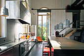 Küchenzeile und Kücheninsel mit Barhockern vor geöffneter Fenstertür in umgebautem Loft