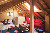 Rotes Sofa, Hocker mit Tierfell und Schaukelpferd im Dachzimmer mit Holzverkleidung