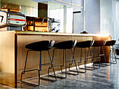 Kitchen island made of polished brass with bar stools in an elegant, open living room with marble tiles