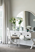 White dressing table against large, round mirror on wall