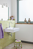 Sink mounted on green wall tiles and stool in bathroom