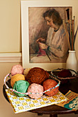 Balls of wool in wire basket, knitting needles and picture of knitting woman