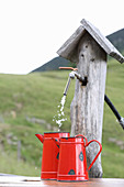 Water running from wooden pump into red enamel jugs
