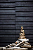 Stylized Christmas tree made of jute loops and driftwood sticks in front of a wooden wall on a terrace