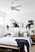 Double bed against ledge in wood panelling in white bedroom with ceiling fan