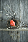Handbemaltes rotes Osterei in Weidennest mit Kätzchenzweigen auf Holzregal