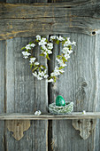 Wreath of cherry blossom and hand-painted green Easter egg on shelf on rustic wooden wall