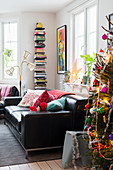Weihnachtsbaum, schwarzes Ledersofa, Stehlampe und Bücherregal im Wohnzimmer
