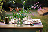 Gedeckter Tisch mit Blumen in Apothekerflaschen im Garten