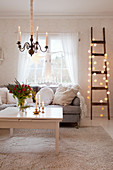 Ladder decorated with fairy lights next to grey sofa in living room