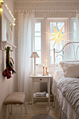 Bedside table and bed in front of window in bedroom decorated for Christmas