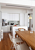 Wooden table and white classic chairs, kitchen counter and white fitted kitchen in open-plan interior