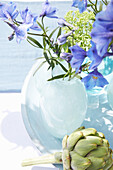 Blue delphinium flowers in glass vase, artichoke in front of it