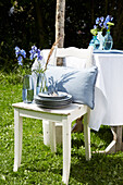 Wooden chair with blue cushion and delphinium in front of table in the garden