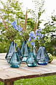Blue glass vases with artichokes and delphiniums on a wooden table in the garden