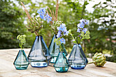 Blue glass vases with artichokes and delphiniums on a wooden table in the garden