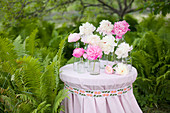 Peonies in glass bottles on table amongst ferns