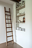 Wooden ladder against white wall next to shelves of crockery
