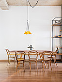 Dining table and bentwood chairs below pendant lamp with small yellow lampshades