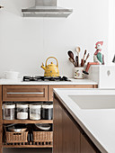 Blick über Kücheninsel auf Unterschrank mit Vorratsbehältern und Gasherd mit Wasserkessel