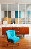 Blue easy chair and retro sideboard against glass partition wall