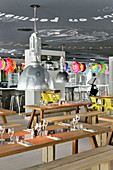 Wooden tables and benches in restaurant; colourful rubber rings above bar in background