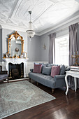 Grey sofa, gilt-framed mirror above fireplace and stucco ceiling in elegant living room