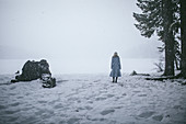 Frau in hellblauem Mantel am Ufer eines zugefrorenen Sees bei Schneefall