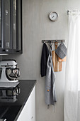 Kitchen utensils hung from row of hooks on pale grey wall next to kitchen counter