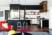 Black and white wall tiles in an open kitchen with an island, in the foreground a red armchair