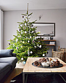 Geschmückter Weihnachtsbaum, Tablett mit Weihnachtsdekoration auf Couchtisch und Polstercouch im Wohnzimmer