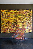 Metal chair with colourful beaded seat and arms in front of painting