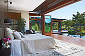 Doppelbett im Schlafzimmer mit offener Terrassentür, Blick auf Pool im Garten