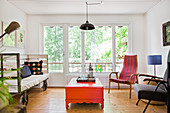 Vintage Sofa auf Rädern, orangefarbener Couchtisch und verschiedene Stühle im Wohnzimmer